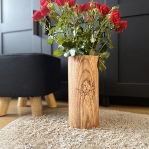 May include: A wooden vase with a floral design carved into the side. The vase is filled with a bouquet of red roses.