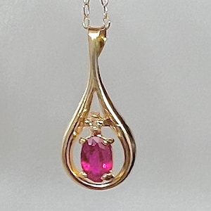 Könnte beinhalten: Eine goldene Anhängerkette mit einem tropfenförmigen Rahmen, der einen einzelnen oval geschliffenen, leuchtend rosa Edelstein umschließt. Der Anhänger hängt an einer zarten Goldkette und besticht durch ein poliertes Metallfinish und eine sichere Krappenfassung.