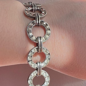 Peut inclure: Un bracelet en argent avec une chaîne de cercles entrelacés, chaque cercle est incrusté de strass transparents.