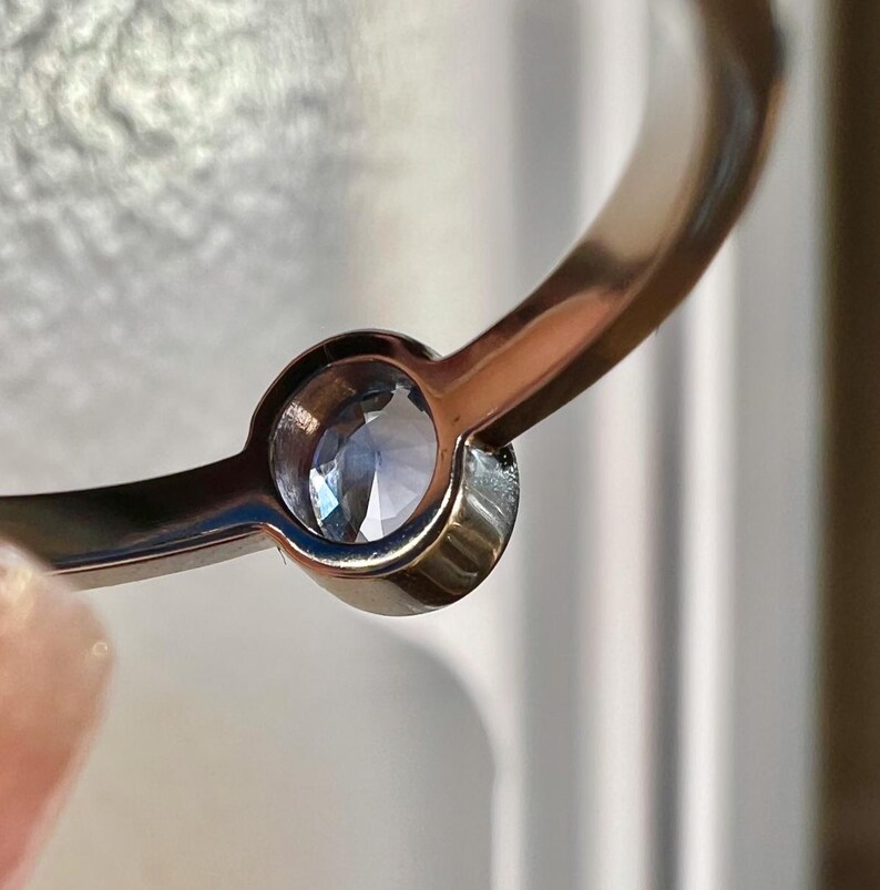 Pu&ograve; includere: Primo piano di un anello in oro rosa con una singola pietra preziosa trasparente incastonata in una montatura a castone.