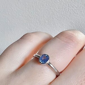 Pu&ograve; includere: Un anello d'argento con una pietra preziosa blu incastonata in una montatura a  bezel.