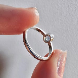 Pu&ograve; includere: Un anello d'argento con una pietra preziosa trasparente incastonata in una montatura a castone. L'anello &egrave; semplice ed elegante.