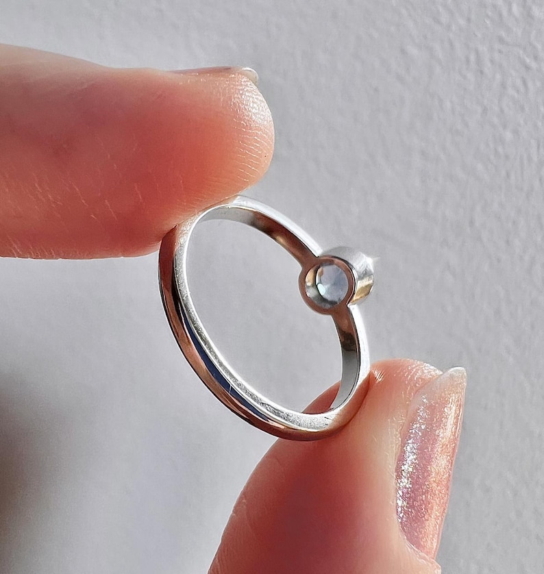 Pu&ograve; includere: Un anello d'argento con una pietra preziosa trasparente incastonata in una montatura a castone. L'anello &egrave; semplice ed elegante.
