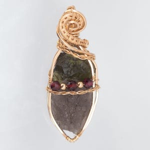 May include: A gold-coloured wire-wrapped pendant with a dark green and grey stone. Three small, round, red beads are set in the middle. The top of the pendant has a decorative swirl design.
