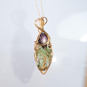 以下が含まれることがあります： 緑と紫の宝石に木がデザインされた、金色のワイヤーで包まれたペンダント。
