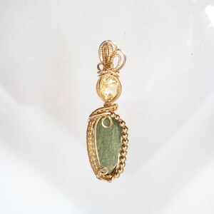 May include: A gold pendant featuring a light green, oval-shaped stone, a yellow gemstone, and intricate wire wrapping. The pendant is suspended from a gold bail. The design showcases a combination of natural elements and craftsmanship.