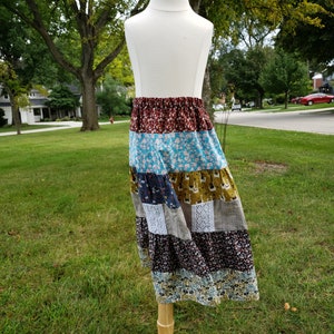 Peut inclure: Une jupe patchwork multicolore avec une variété de motifs floraux et géométriques. La jupe est faite de différents tissus, dont du coton et de la dentelle. Elle est exposée sur un mannequin en bois.