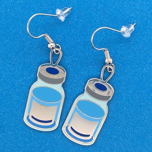 May include: A pair of silver earrings with blue and gray glass vial charms. The vials have a silver cap and a blue liquid inside.