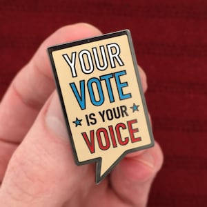 May include: A speech bubble shaped enamel pin with the text "YOUR VOTE IS YOUR VOICE" in white, blue, and red lettering with two stars on either side of the text "IS YOUR".
