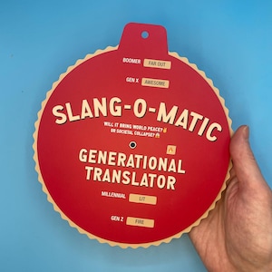 May include: A red and tan circular game piece with the text "SLANG-O-MATIC" and "GENERATIONAL TRANSLATOR". The game piece has a dial with different slang terms for each generation, including Boomer, Gen X, Millennial, and Gen Z.