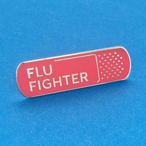 May include: A red and silver enamel pin shaped like a bandage with the text "FLU FIGHTER" in white lettering.