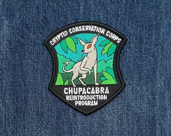 Puede incluir: Parche bordado negro y verde con una criatura blanca con ojos rojos. El parche dice "Cryptid Conservation Corps" y "Chupacabra Reintroduction Program".