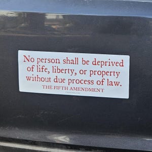 May include: A rectangular white sticker with red text adhered to a gray surface. The text reads: "No person shall be deprived of life, liberty, or property without due process of law." Below, it says "THE FIFTH AMENDMENT" and "DISSENTPINS.COM".