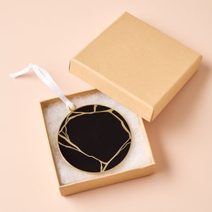 May include: A round black and gold ornament with a crackled design, in a brown box with white padding.