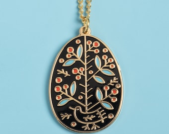 May include: Gold-tone necklace with a black oval pendant. The pendant features a stylized tree design with red berries and blue leaves, and a bird at the bottom. The necklace is on a light blue background.
