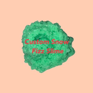 May include: A vibrant green slime with a textured, snow-like appearance. The words "Custom Snow Fizz Slime" are written in red across the center of the slime, set against a peach-colored background. This product is likely a sensory toy.