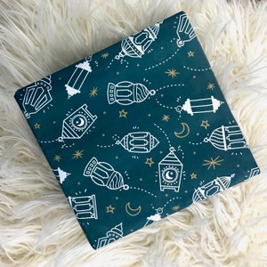 Puede incluir: Papel de regalo azul verdoso con un patr&oacute;n blanco de linternas y estrellas. Las linternas tienen un dise&ntilde;o de luna creciente y est&aacute;n conectadas por l&iacute;neas punteadas.