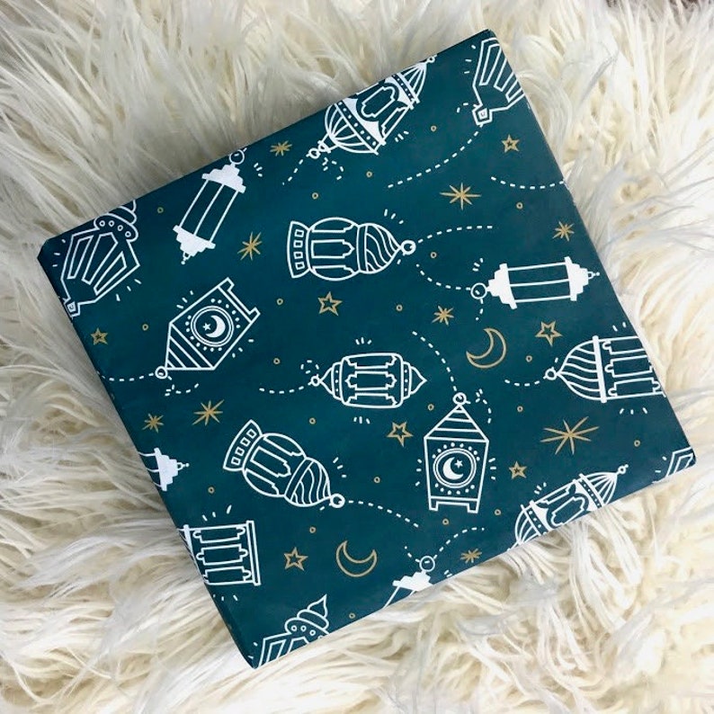 Puede incluir: Papel de regalo azul verdoso con un patr&oacute;n blanco de linternas y estrellas. Las linternas tienen un dise&ntilde;o de luna creciente y est&aacute;n conectadas por l&iacute;neas punteadas.