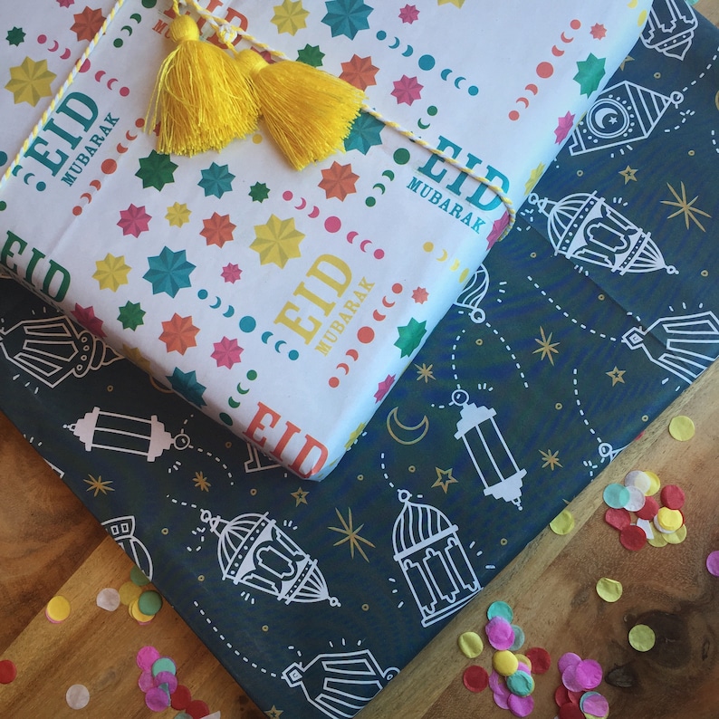 Puede incluir: Dos hojas de papel de regalo con dise&ntilde;os diferentes. Una hoja es blanca con estrellas de colores, medias lunas y el texto "Eid Mubarak". La otra hoja es azul oscuro con estrellas blancas, medias lunas y linternas.