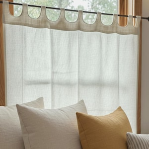 a cozy and inviting living space with a window, white curtains, and a comfortable couch adorned with three pillows in various colors and patterns.