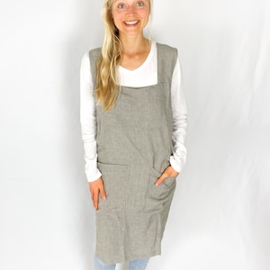 May include: A long, grey and white striped apron with a large pocket on the front. The apron is worn over a white long-sleeved shirt and blue jeans.