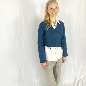 May include: A blue quilted wrap jacket with a tie closure. The jacket is cropped and has a relaxed fit. The model is wearing a white shirt and brown pants.