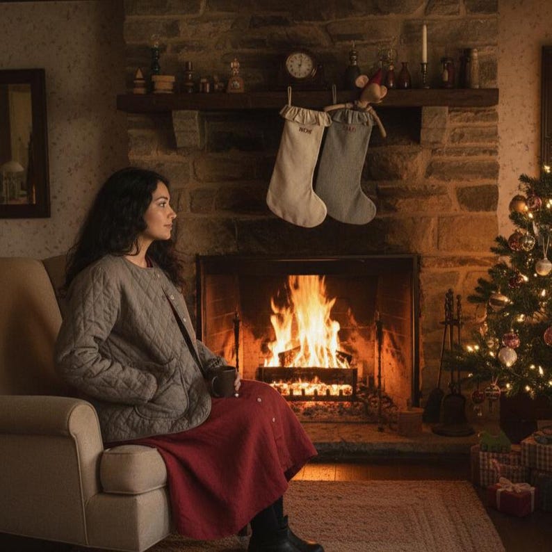 Puede incluir: Una acogedora escena navide&ntilde;a con chimenea, &aacute;rbol y calcetines. Una persona est&aacute; sentada en una silla, con una chaqueta acolchada y una falda roja, sosteniendo una taza. La chimenea tiene un fuego crepitante y la habitaci&oacute;n est&aacute; decorada para las fiestas.