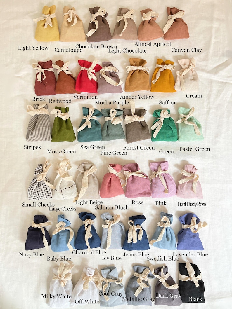 May include: A collection of small fabric drawstring pouches arranged in rows, each tied with a cream-colored ribbon. The pouches come in a wide variety of solid colors, including yellow, brown, red, green, blue, pink, gray, and black, plus some patterned options.