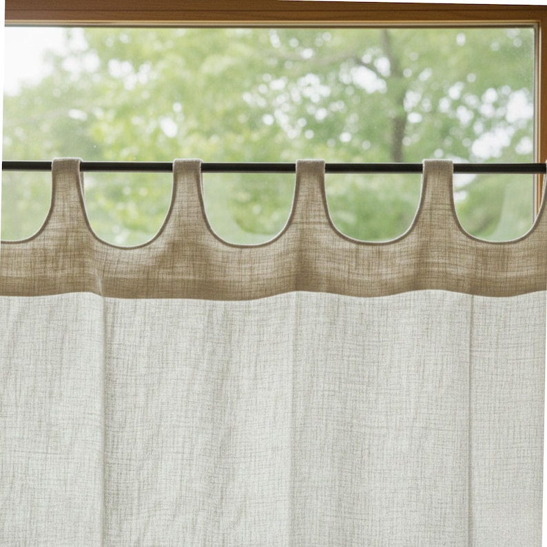 a window with a curtain hanging from a rod, featuring a beige fabric with a textured pattern. The curtain appears to be made of a soft, natural material, and the window is framed in wood. The background of the image is a blurred view of trees, suggesting that the window is located in a natural setting.