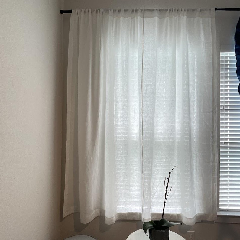 a window with white curtains, a small potted plant, and a white wall in the background.