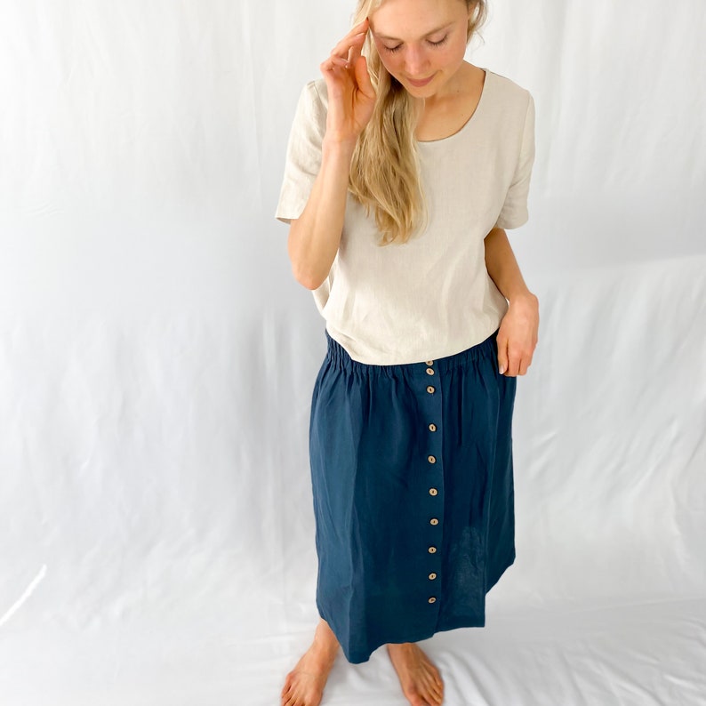 May include: A dark blue linen skirt with a button-up front and an elastic waistband. The skirt is knee-length and has a relaxed fit.