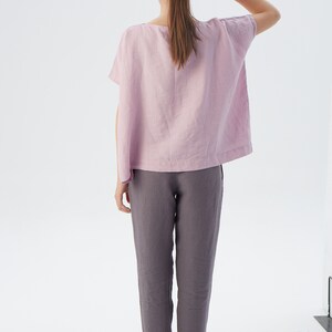 May include: A woman wearing a light pink linen top with short sleeves and a pair of gray linen pants.