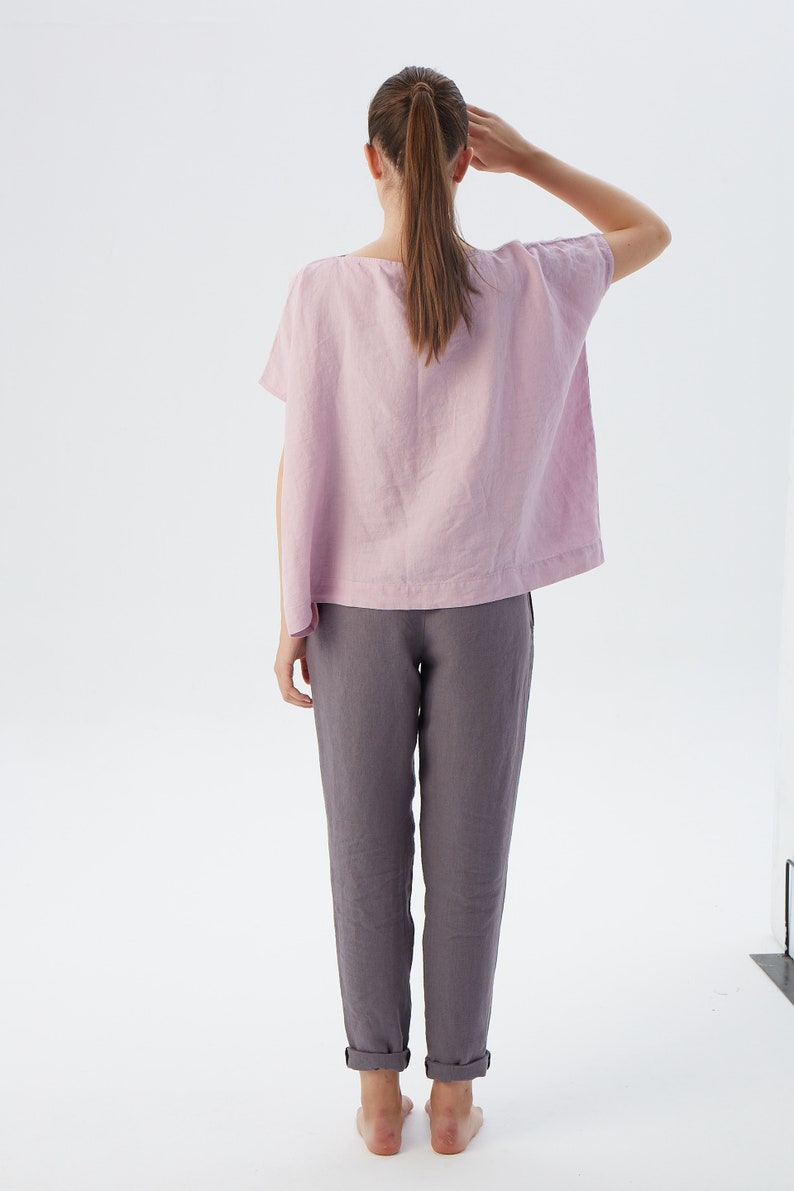 May include: A woman wearing a light pink linen top with short sleeves and a pair of gray linen pants.