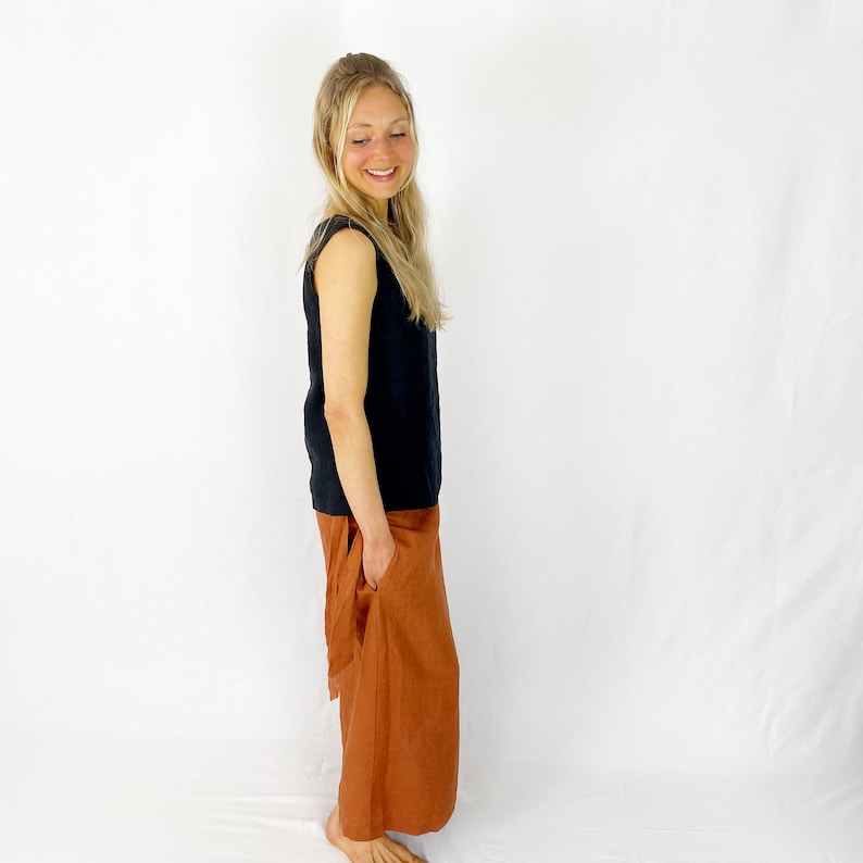 May include: A woman wearing a black sleeveless top and a rust-colored linen skirt with a pocket. The skirt is gathered at the waist and falls to the ankles.