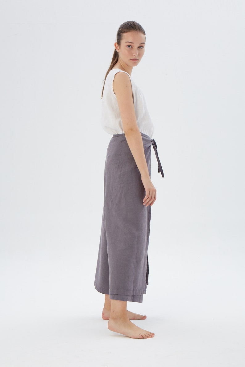 Puede incluir: Una mujer con una camiseta sin mangas blanca y una falda envolvente gris. La falda se ata a la cintura con una cinta de tela a juego. El conjunto est&aacute; hecho de una tela ligera, adecuada para el clima c&aacute;lido.