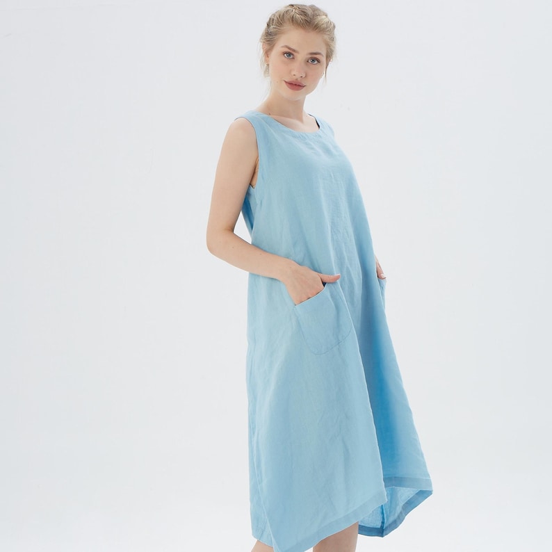 May include: A light blue sleeveless linen dress with two pockets. The dress has a loose fit and a slightly asymmetrical hemline.