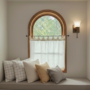 a cozy corner of a room with a window, a light fixture, and a bench with pillows.