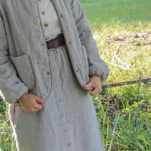 May include: A light green corduroy jacket, dress, and shirt set. The jacket has a round collar, pockets, and button closures. The dress is button-down with a matching corduroy texture. A brown belt cinches the waist. The outfit is suitable for casual wear.