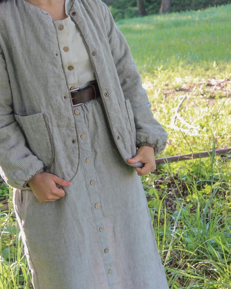 May include: A light green corduroy jacket, dress, and shirt set. The jacket has a round collar, pockets, and button closures. The dress is button-down with a matching corduroy texture. A brown belt cinches the waist. The outfit is suitable for casual wear.