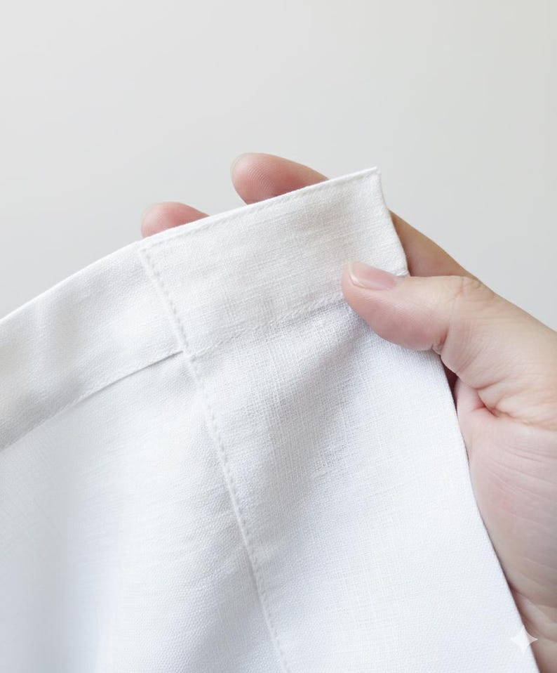 A hand is holding a white fabric, possibly a piece of clothing or a textile, with the fabric folded in half.