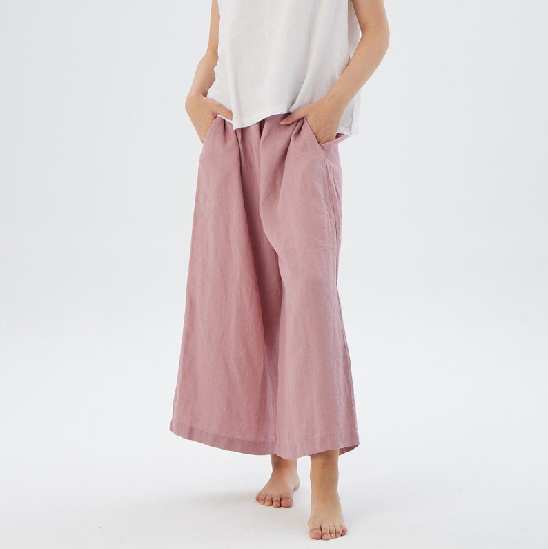 Puede incluir: Un pantal&oacute;n de lino de color rosa polvoriento de pierna ancha con un ajuste holgado. El pantal&oacute;n tiene una cintura alta y est&aacute; hecho de una tela ligera y transpirable.