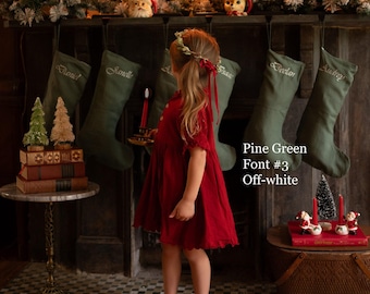 May include: A set of pine green stockings hanging from a fireplace mantel, each embroidered with a name in off-white thread. The text Pine Green, Font #3, and Off-white is visible. The stockings are made of fabric and feature a simple design.