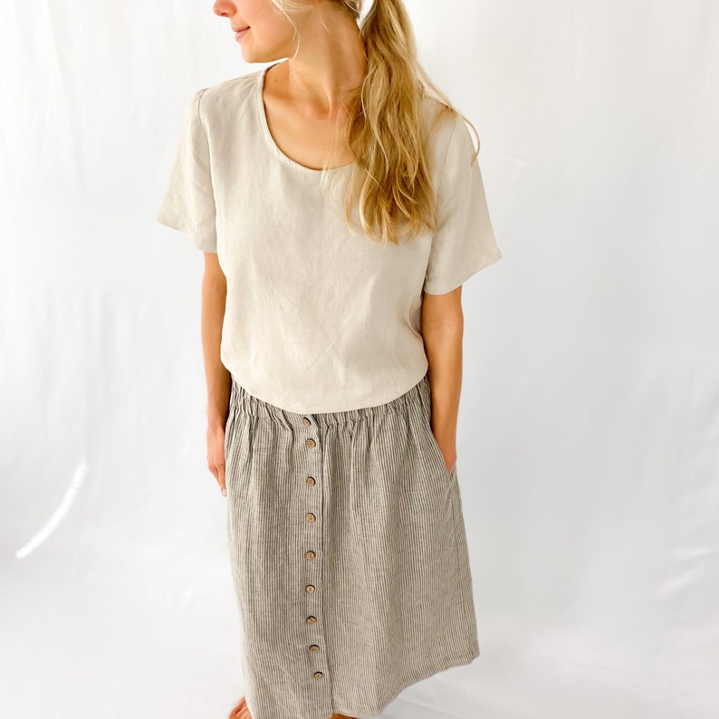 May include: A beige linen top with a scoop neck and short sleeves paired with a striped linen skirt with a button front.
