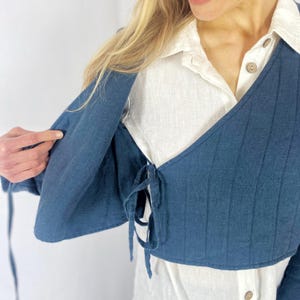 May include: A dark blue linen wrap top with a tie closure at the waist. The top is worn over a white linen shirt.