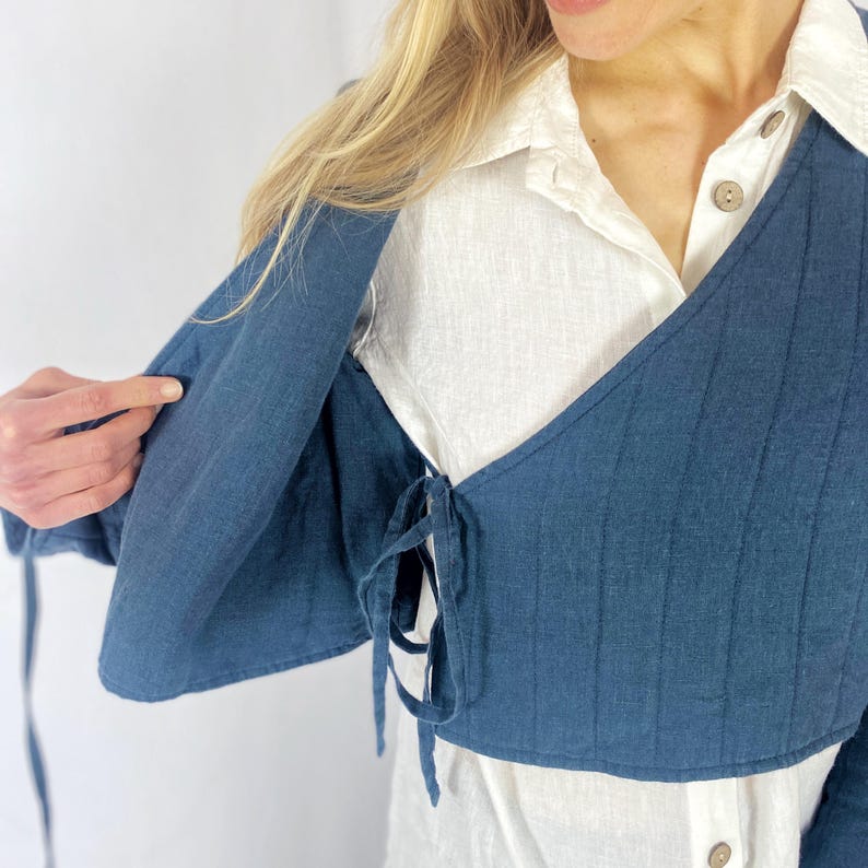 May include: A dark blue linen wrap top with a tie closure at the waist. The top is worn over a white linen shirt.