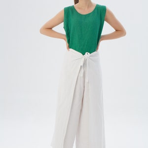 May include: A sleeveless emerald green top with a round neckline paired with white wide-leg wrap pants that feature a front tie closure at the waist. The ensemble is crafted from a textured fabric and provides a loose, comfortable fit.