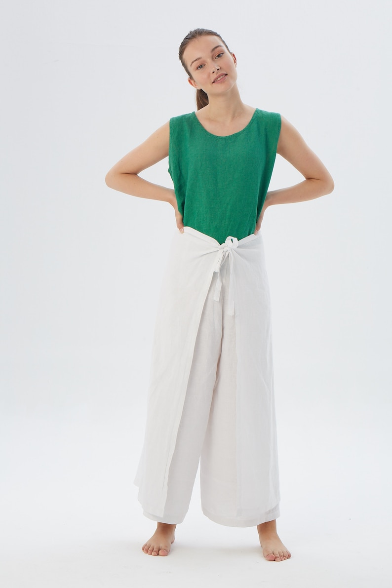 May include: A sleeveless emerald green top with a round neckline paired with white wide-leg wrap pants that feature a front tie closure at the waist. The ensemble is crafted from a textured fabric and provides a loose, comfortable fit.
