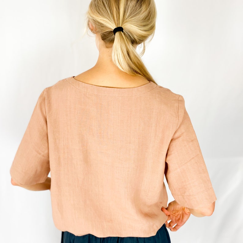 May include: A light pink linen top with a scoop neck and short sleeves. The top is loose fitting and has a relaxed silhouette.