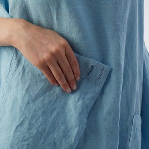 May include: A light blue linen tunic with a patch pocket and two small holes on the pocket flap.