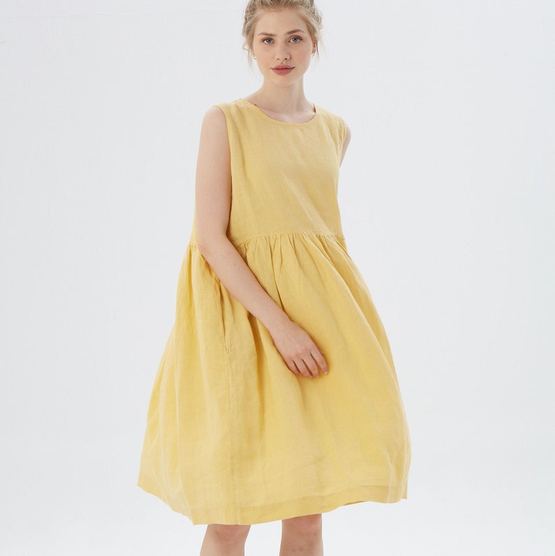May include: A sleeveless, yellow dress with a round neckline and a gathered waist. The dress has a loose, flowing skirt and is made of a lightweight fabric. The model is wearing the dress in a studio setting with a white background.